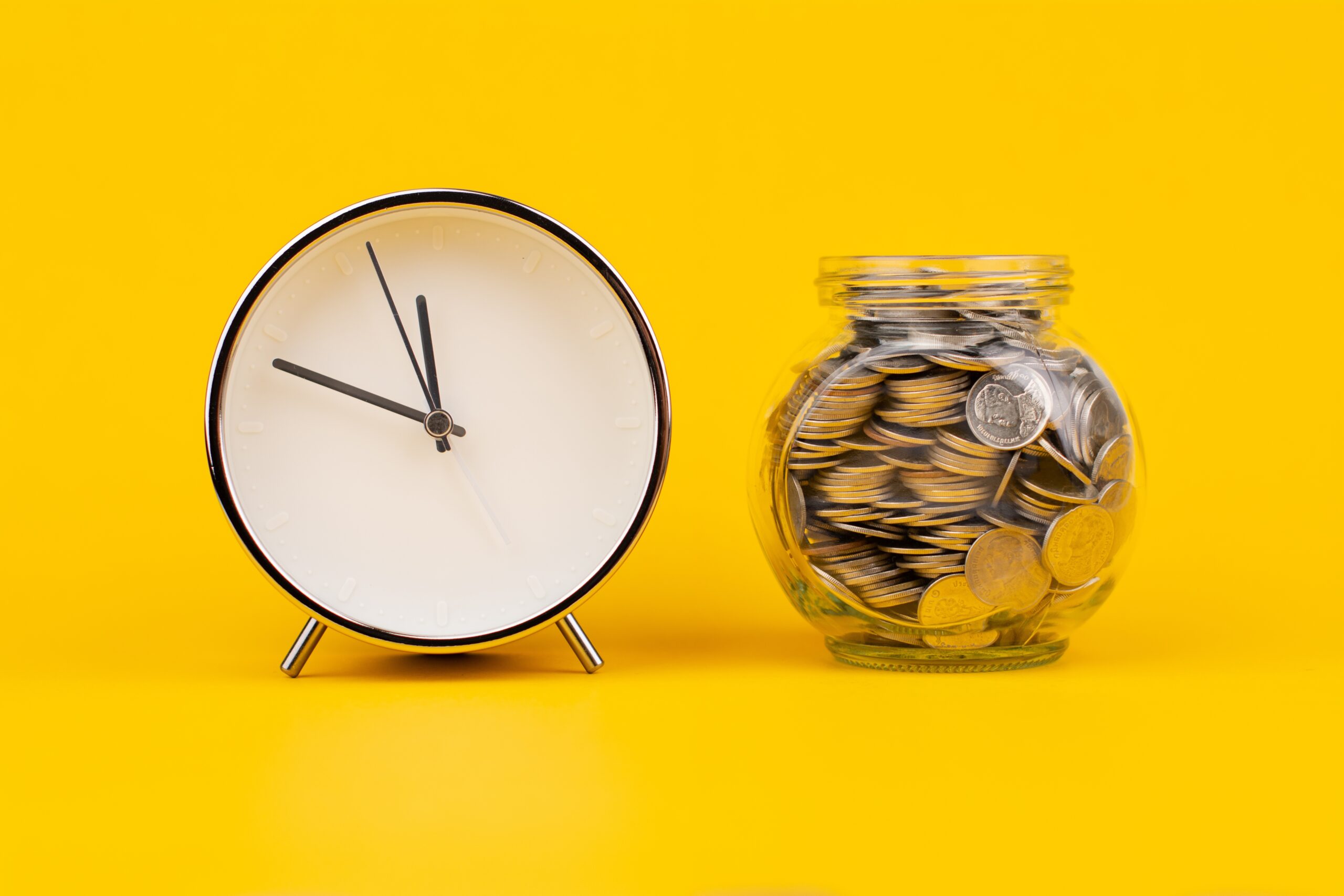 A glass jar of coins next to a clock, symbolizing how time can impact revenue